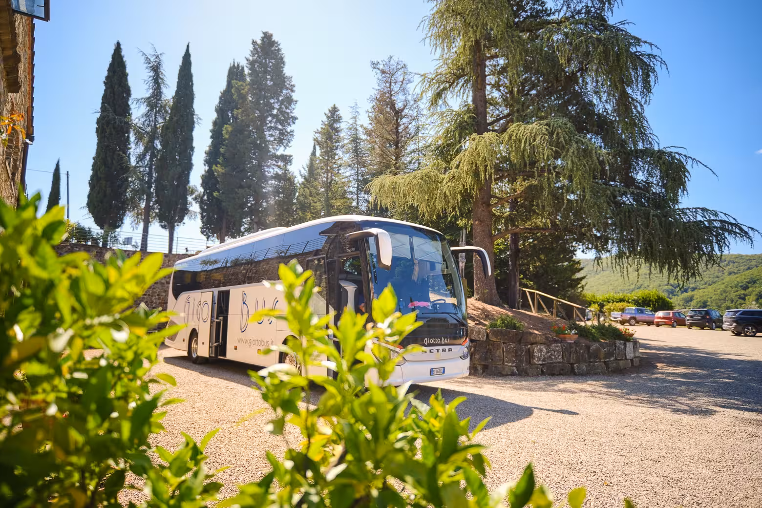 Tour bus parked amidst the serene Chianti countryside, surrounded by lush trees under a bright sky.