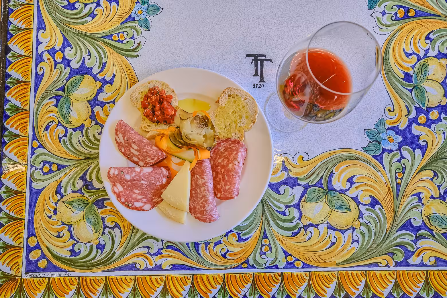Plate of Italian antipasto with salami, cheese, and wine on a colorful table in Chianti winery tour.