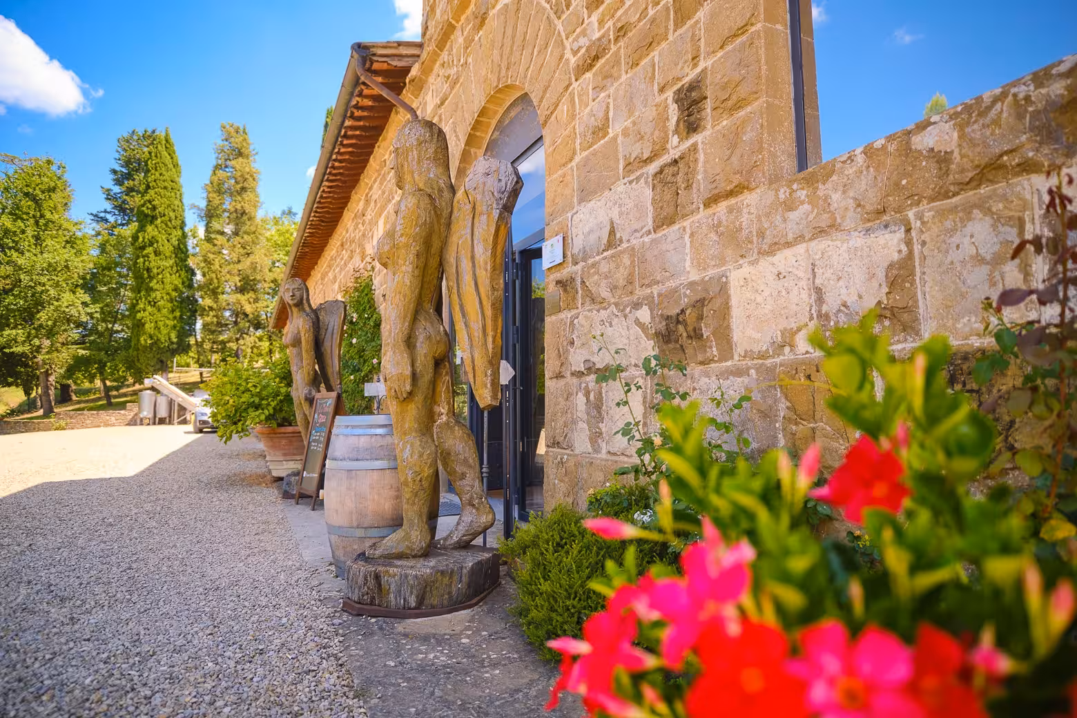 Stone building with wooden sculptures and vibrant flowers at a Chianti winery, perfect for a Florence half-day tour.