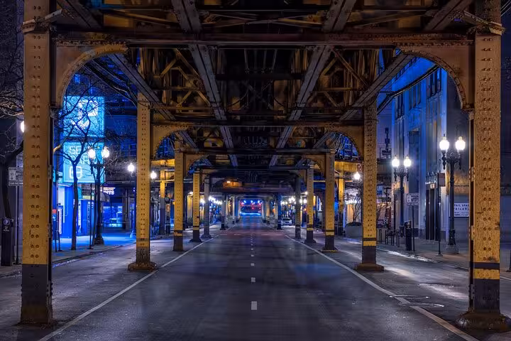 Empty Chicago street at night under elevated train tracks with glowing streetlights and blue-lit buildings
