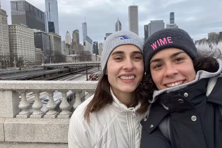 Two smiling women in winter hats taking a selfie with Chicago skyline and Grant Park in background