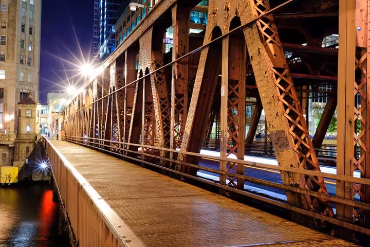 Historic iron truss bridge at night in Chicago with glowing city lights reflecting on wet pavement