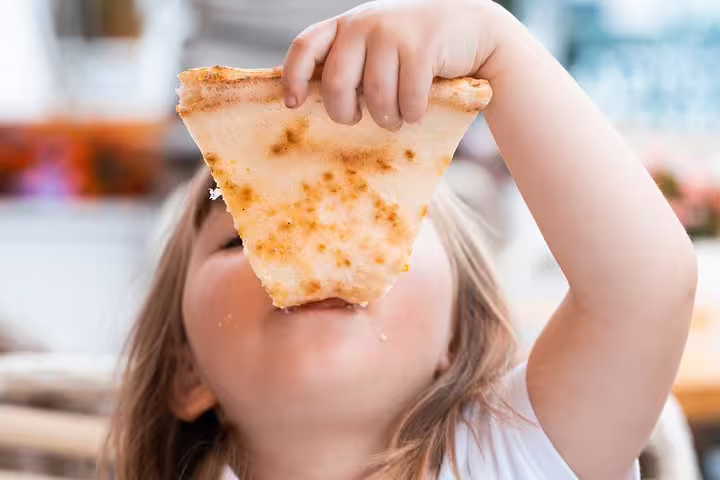 Child enjoying a slice of pizza in Rome during the Bella Roma! Funny Family Private Tour, highlighting games and delicacies for kids.