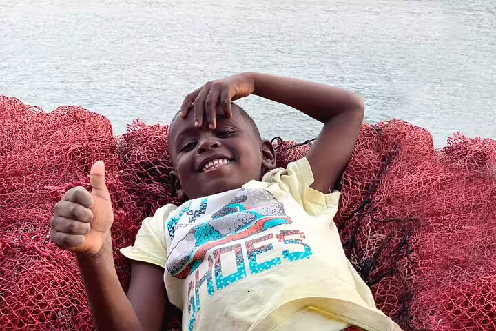 Smiling child giving a thumbs-up while lying on red fishing nets by the sea in Boa Vista, Cape Verde.