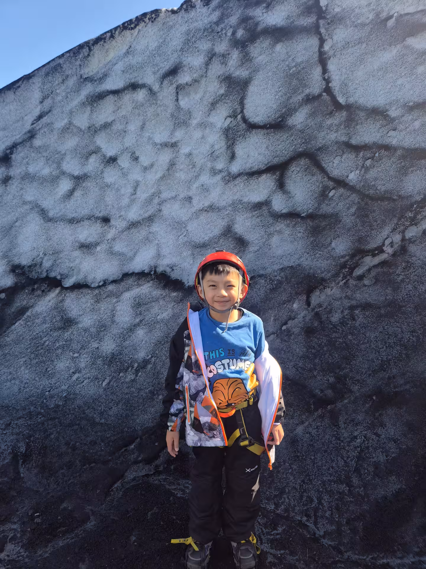 Child in red helmet and harness standing on Iceland glacier during south coast tour
