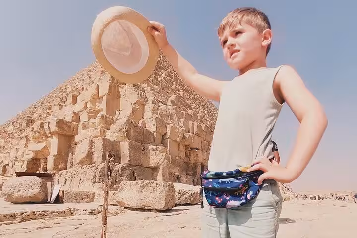 Child visitor poses by the Great Pyramid of Giza on Cairo airport layover tour, desert sightseeing stop