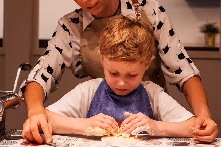 Child learning to make pasta with guidance during an Italian cooking class in Barcelona.