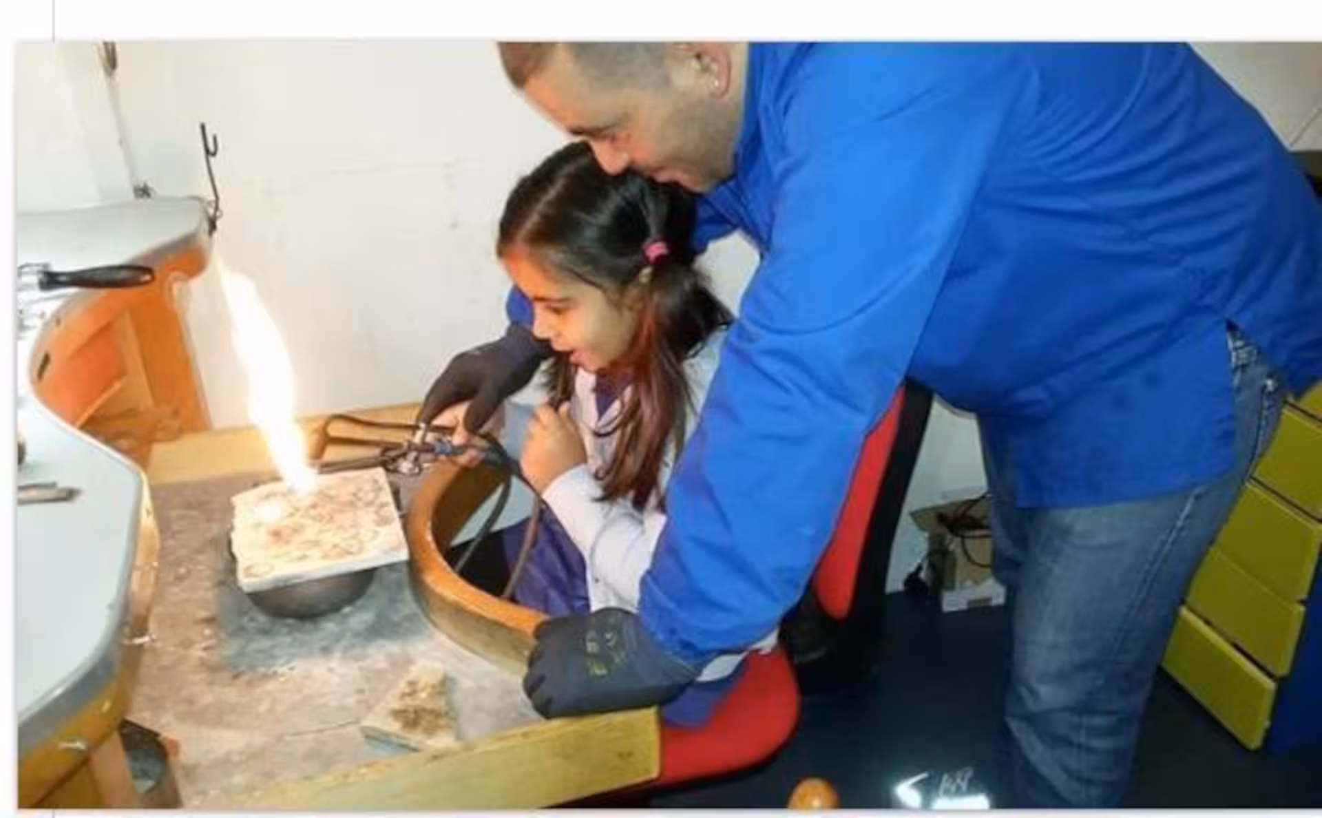 Child learning Sardinian filigree techniques with guidance in Dorgali goldsmith workshop.