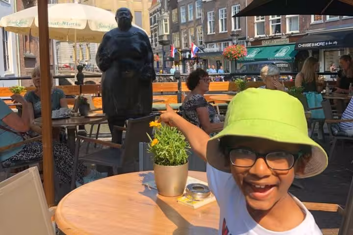 Happy child in green hat pointing at bronze statue at Utrecht outdoor café terrace