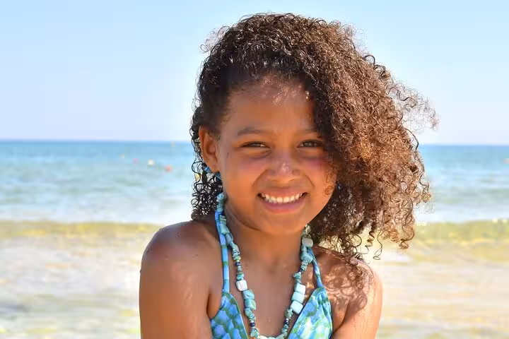 Joyful child in a turquoise mermaid costume smiles brightly on a sunny beach in Hersonissos.