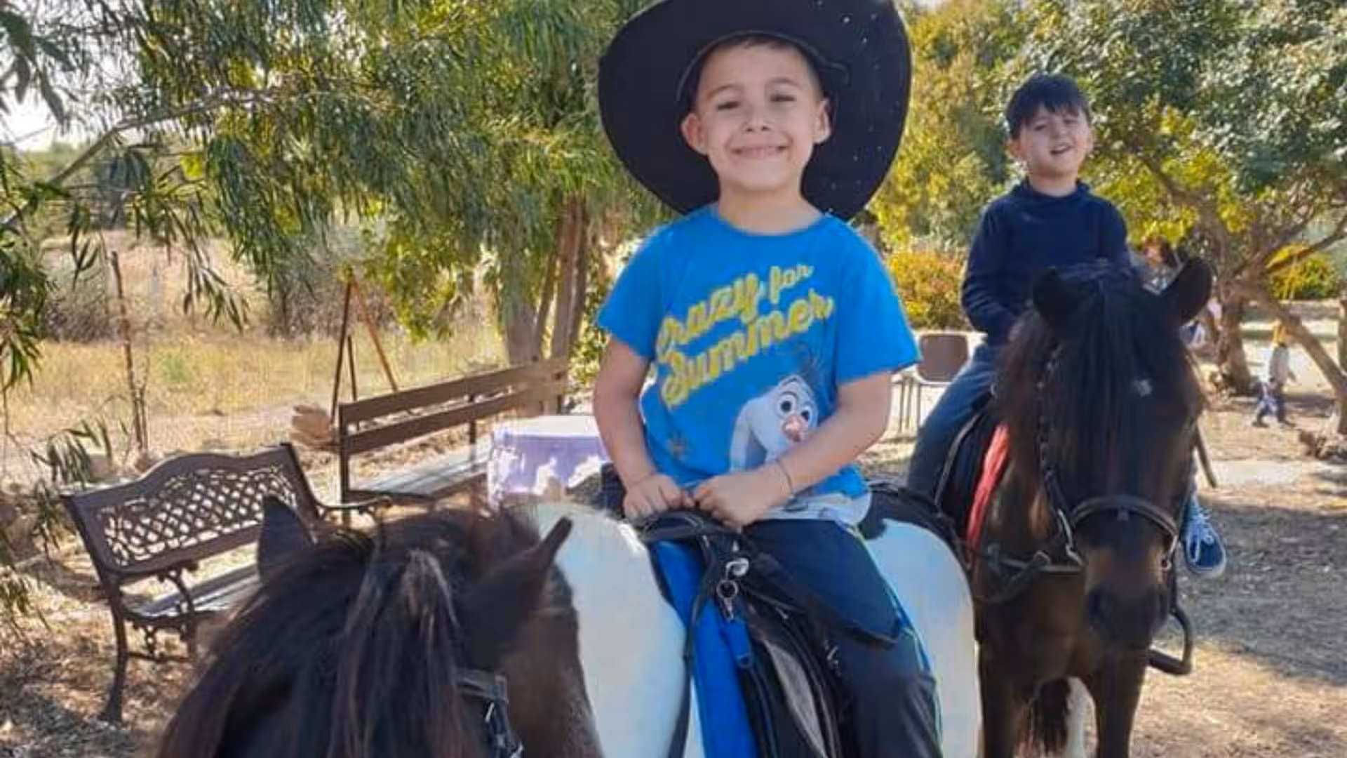 Smiling child in cowboy hat enjoying a pony ride during a Cagliari farm tour.