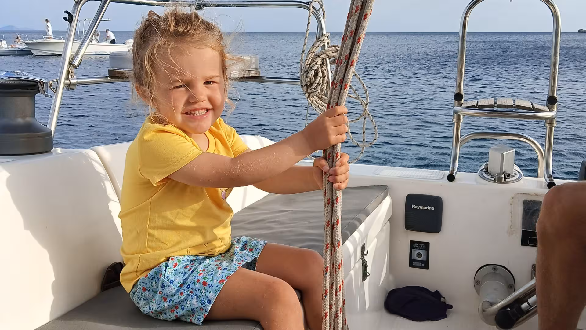 Smiling child enjoys holding ropes on a sailing boat during an Alghero tour, surrounded by serene blue waters.