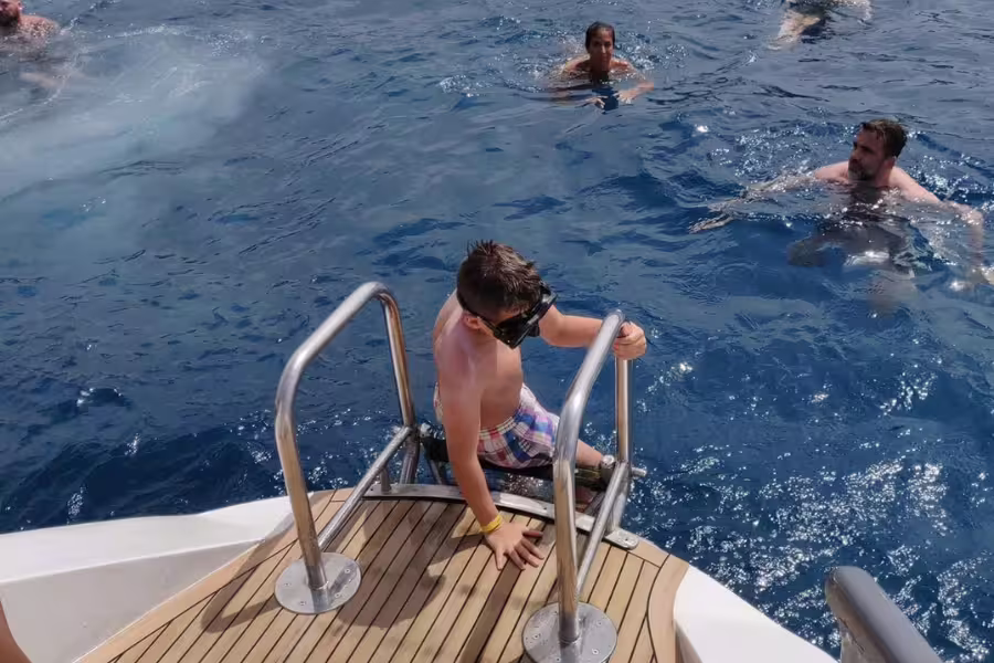 A child with snorkel gear descends from a catamaran into the clear waters, surrounded by swimmers near Masca.