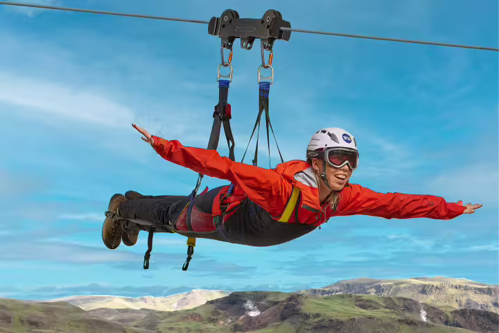 Child enjoying a thrilling Superman zipline ride with arms outstretched above scenic green hills and blue skies.