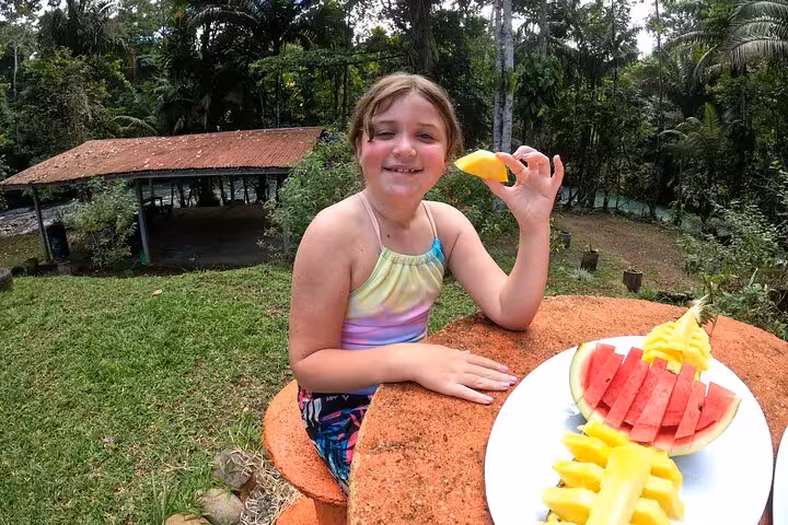Smiling child enjoys fresh tropical fruits amidst lush Rio Celeste scenery on full day hiking and tubing tour.