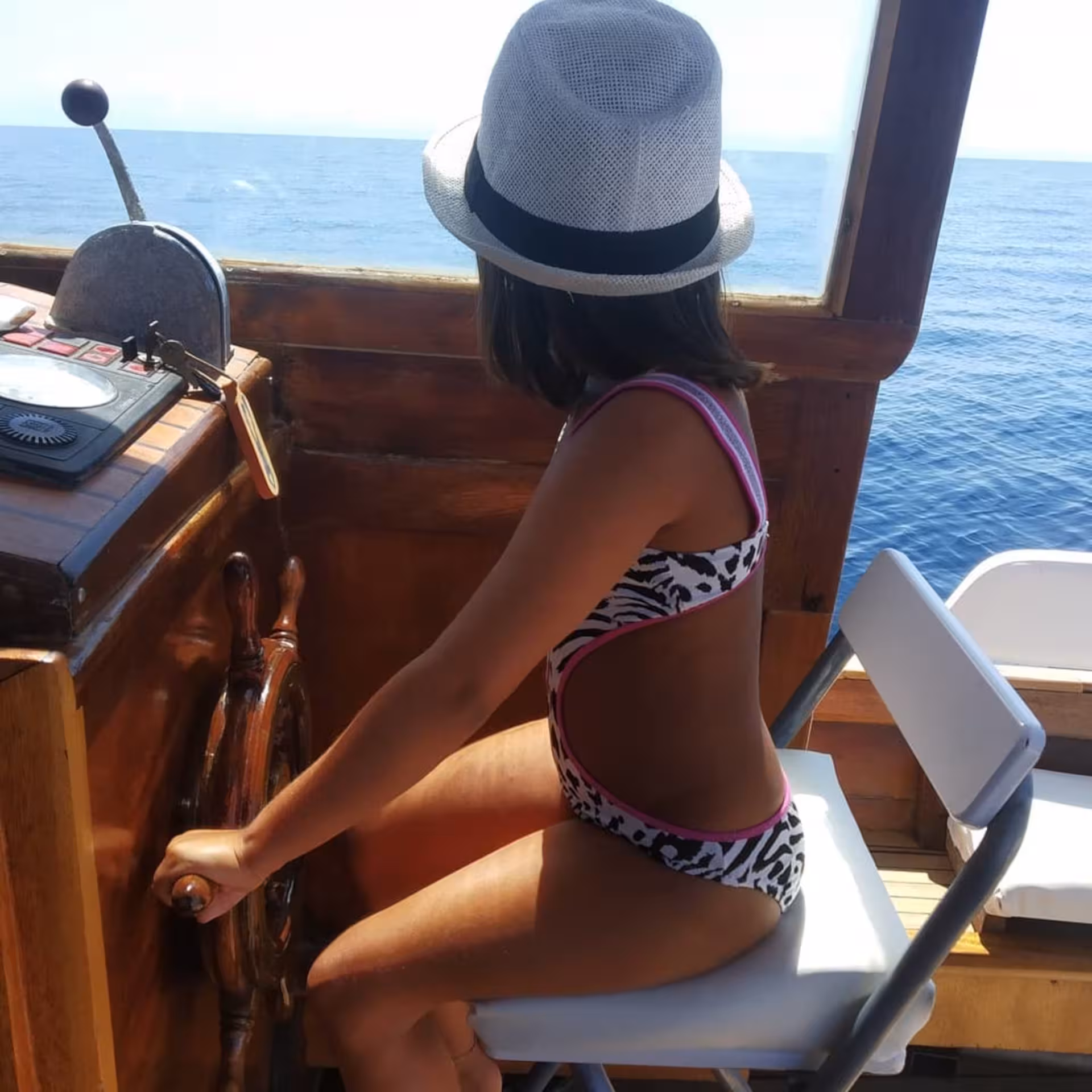 Child steering a wooden boat under clear blue skies on an Asinara Island tour from Stintino.