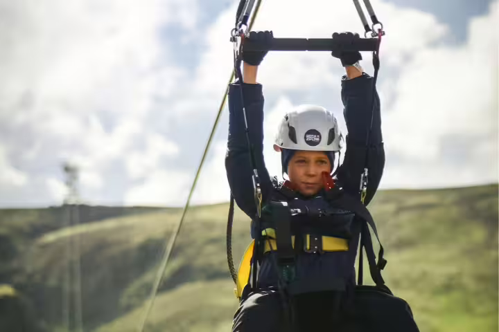 Child enjoying an exhilarating zip line ride over scenic green hills, promoting adventure and outdoor fun for kids.