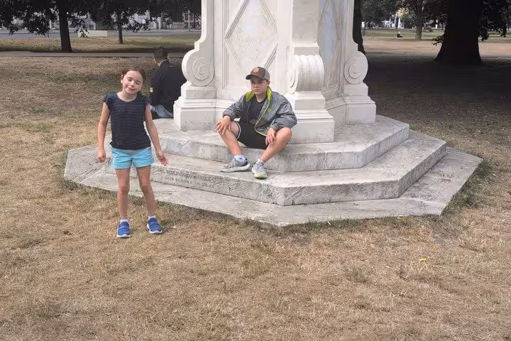 Two children posing at a white stone monument base in Brighton park during self-guided walking tour