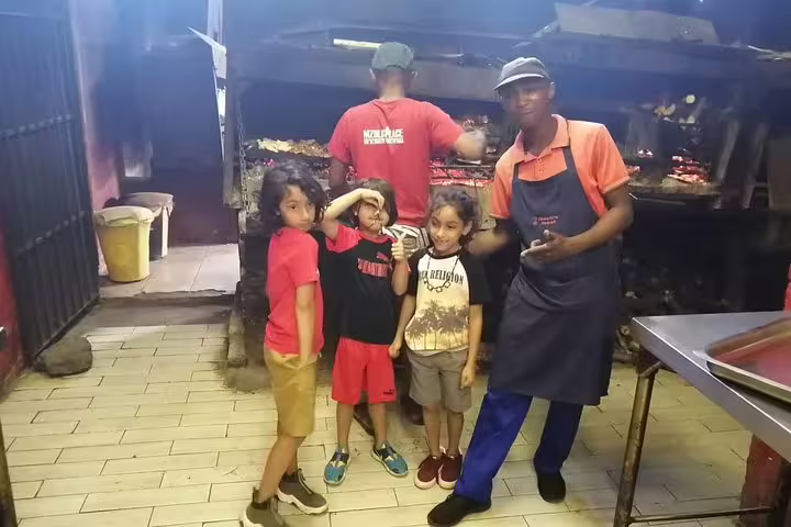 Children posing with chefs in front of wood-fired grills on Langa Township and Bo-Kaap cooking tour.