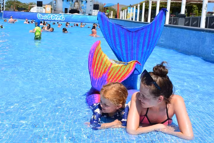 Two children wearing bright mermaid tails playing in a pool under the sun during a fun photoshoot in Hersonissos.