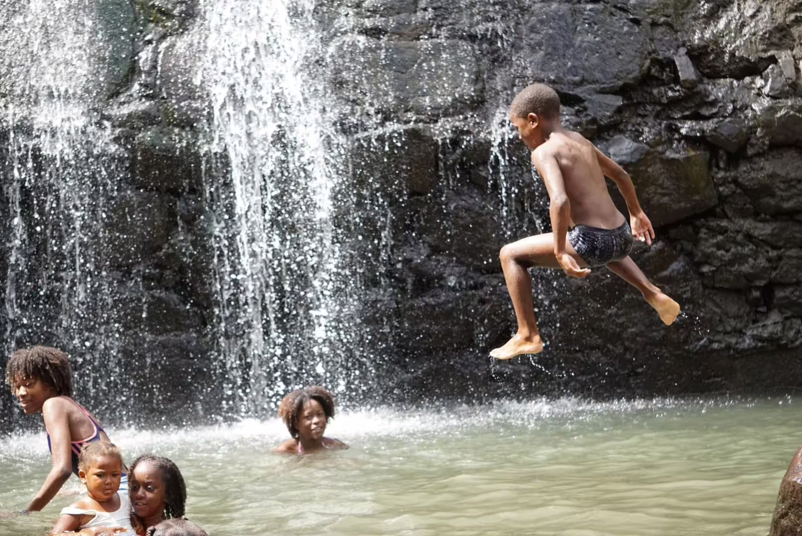 Children joyfully playing and swimming under a refreshing waterfall in the vibrant landscape of Cape Verde.