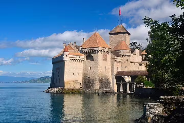 Chillon Castle on Lake Geneva with stone towers and orange rooftops under blue sky, Montreux Switzerland