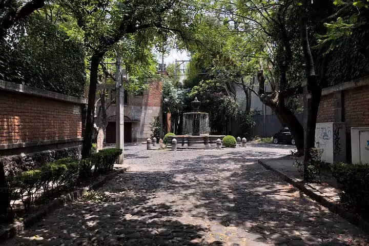 Cobblestone path leading to a stone fountain surrounded by trees and brick walls in Chimalistac, Mexico City