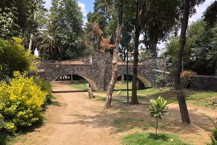 Stone arch bridge surrounded by trees and dirt path in Chimalistac park, Mexico City