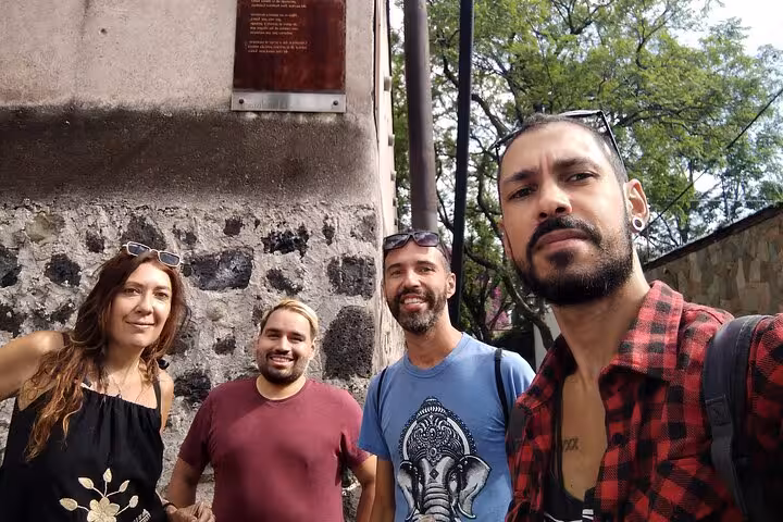 Four travelers posing for a selfie near a historic stone wall and plaque in Chimalistac, Mexico City