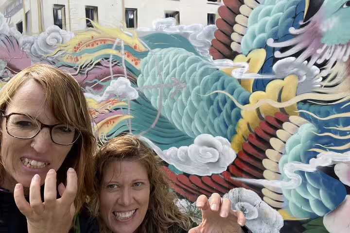 Two women posing and smiling in front of a colorful dragon mural in San Francisco Chinatown