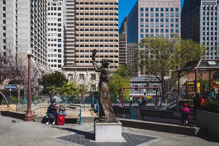 Bronze statue in a San Francisco park near Chinatown with skyscrapers and a Hilton hotel in the background