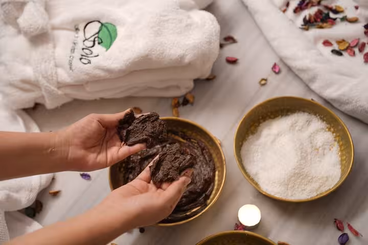 Hands applying chocolate body scrub beside sea salt bowl during Sharm El Sheikh bath spa experience