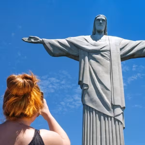 Tourist captures iconic Christ the Redeemer statue against clear blue sky, a highlight of Rio's private tour.