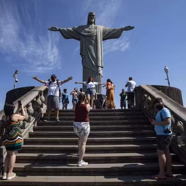 Tourists admire the iconic Christ the Redeemer statue under clear blue skies in Rio de Janeiro, a must-see attraction.