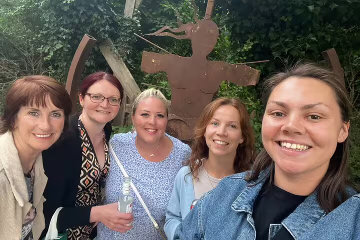 Five women smiling together in front of a rusty metal sculpture surrounded by greenery in Christiania Copenhagen