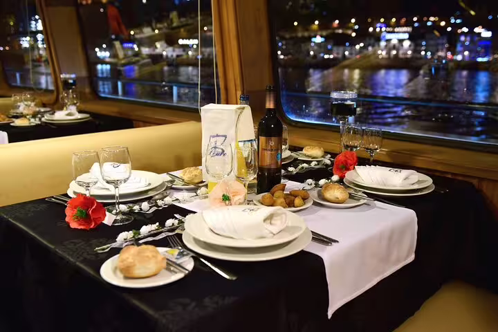 Elegant dining setup on a river cruise with festive decor, wine, and a view of city lights for a Christmas dinner.