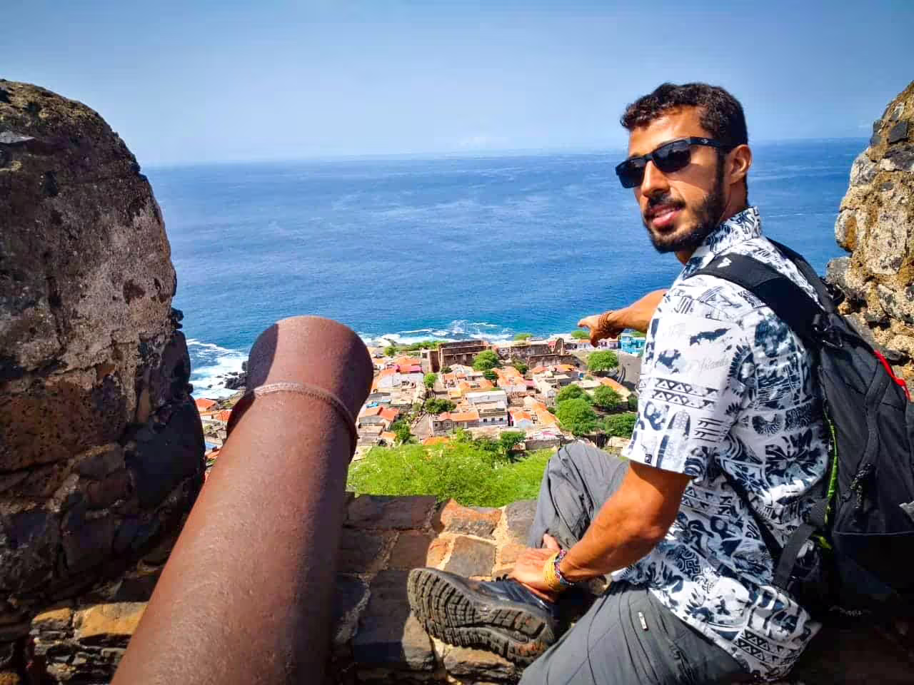 A guide pointing out the coastal view of Cidade Velha from a stone fort with a prominent cannon.