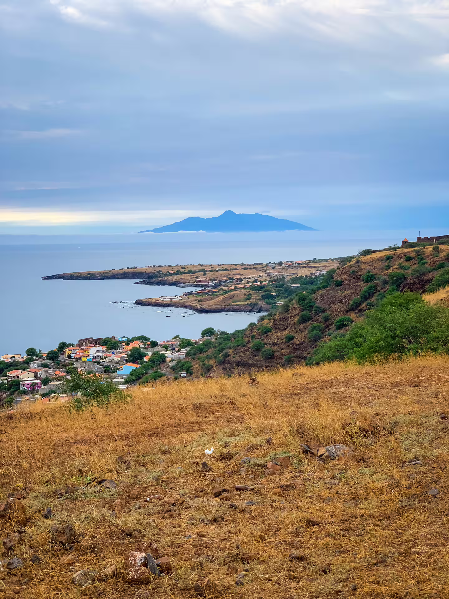 Scenic view of Cidade Velha coastline with lush hills and distant island under a cloudy sky, ideal for guided tours.