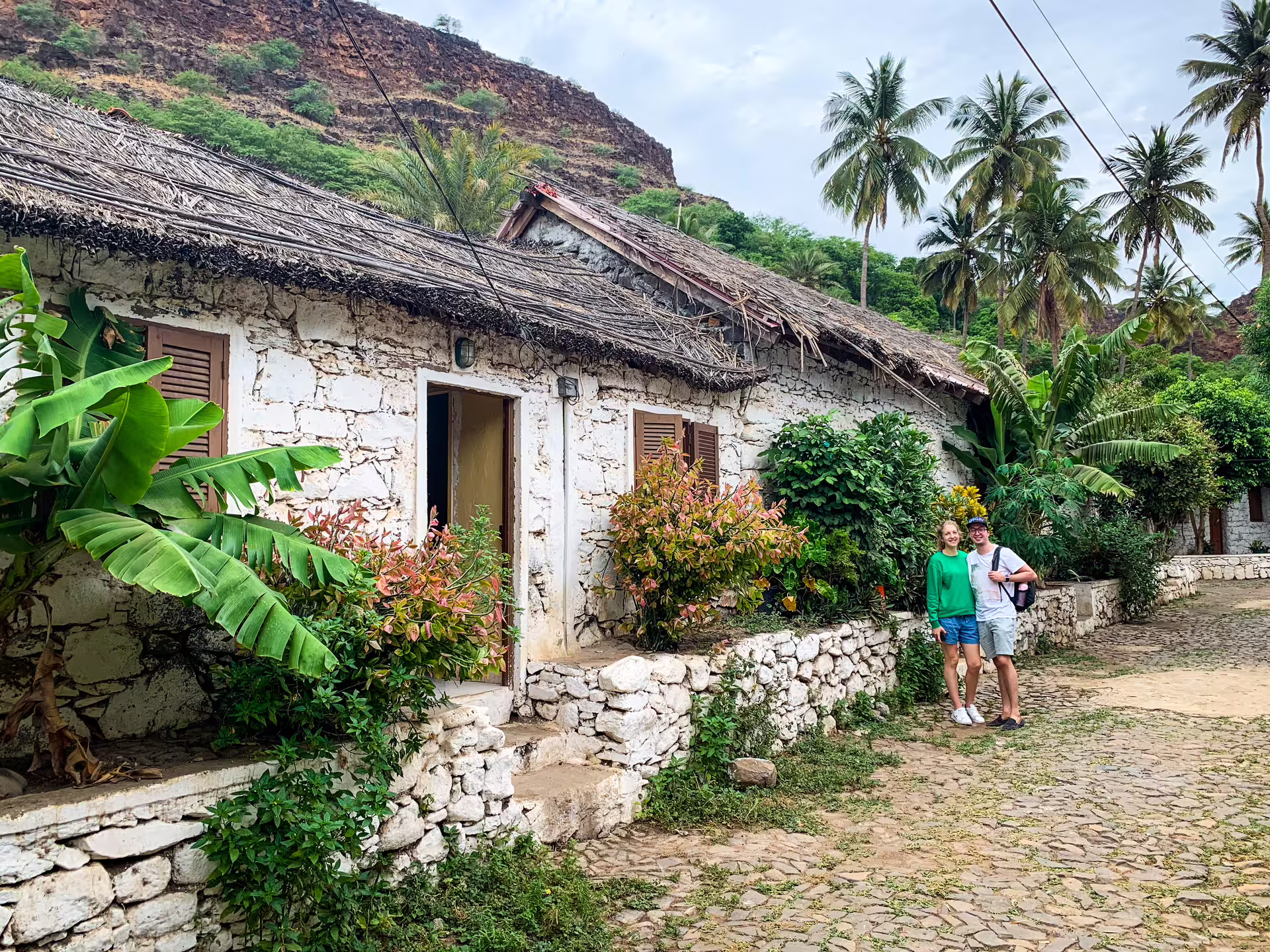 Travelers on cobbled street by traditional thatched house in Cidade Velha village, Santiago Island Praia day tour