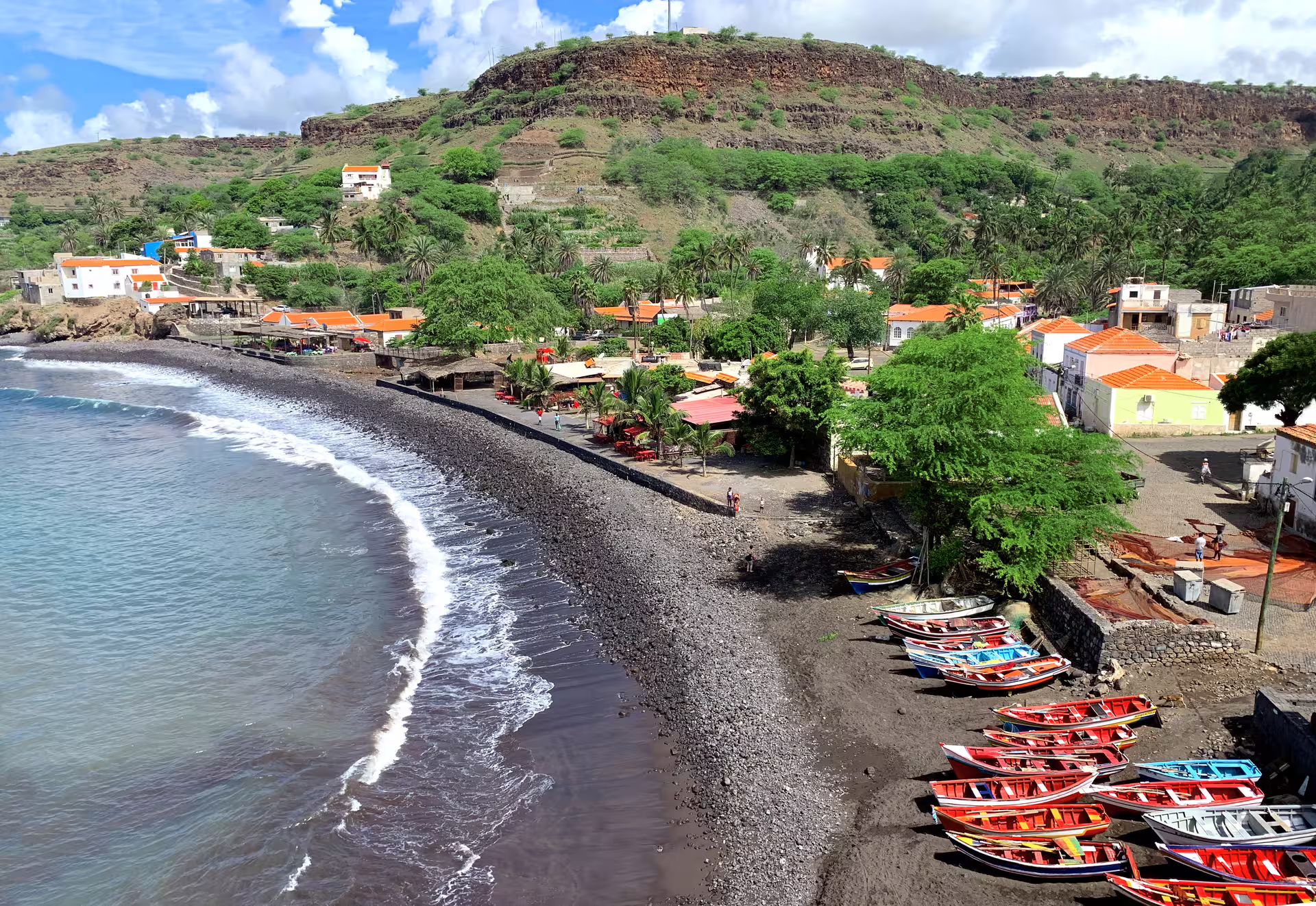 Colorful boats lined on Cidade Velha's rocky beach with lush greenery and vibrant buildings, perfect for cultural exploration.