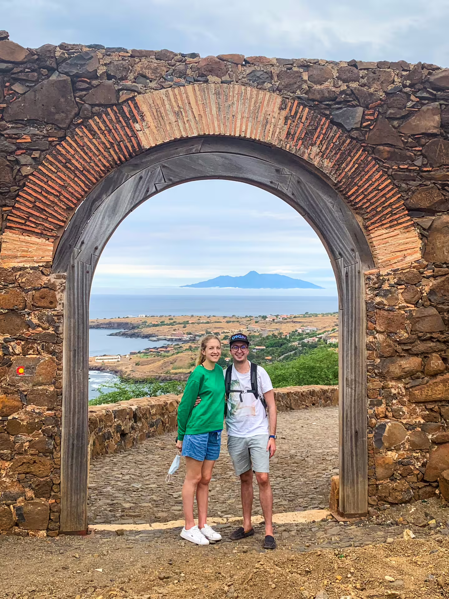 Visitors posing under ancient stone archway with coastal view in Cidade Velha guided tour.