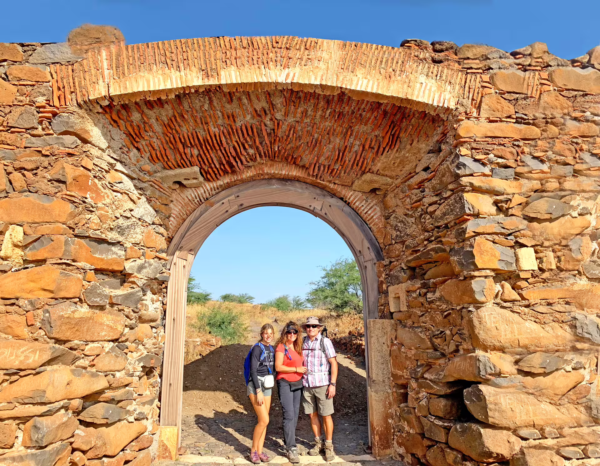 Visitors stand under a rustic stone archway at a historic site in Cidade Velha, Cape Verde.