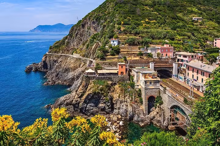 Scenic landscape of Cinque Terre with rugged cliffs, vibrant buildings, and lush greenery by the sea.