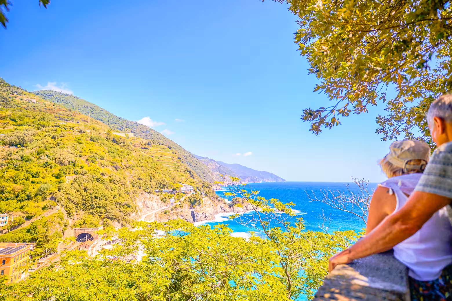 Couple enjoys a panoramic view of the vibrant Cinque Terre coastline with lush hills and azure waters.
