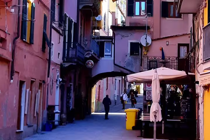 Narrow colorful alley in a Cinque Terre village with cafes, archway and locals enjoying a relaxed walk on a private tour