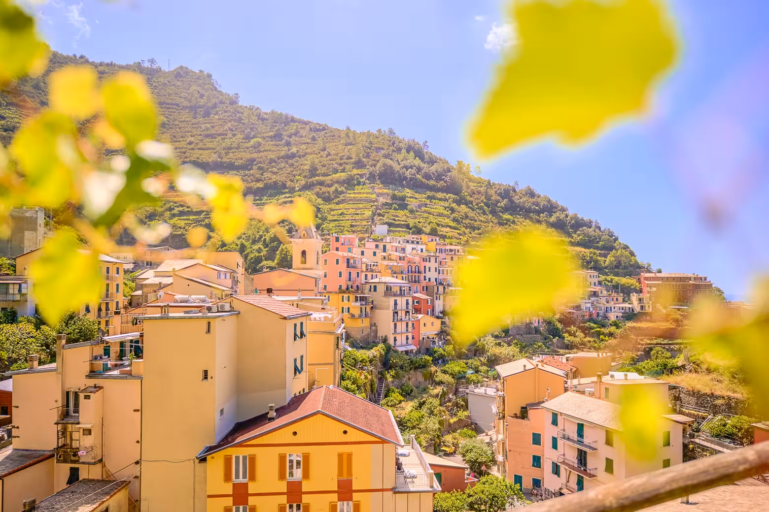 Scenic view of colorful hillside village in Cinque Terre, Italy, surrounded by lush greenery and sunny skies.