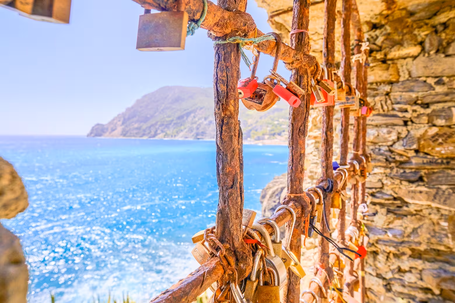 Rustic locks on iron bars overlooking the vibrant blue sea of Cinque Terre, Italy, on a sunny day.