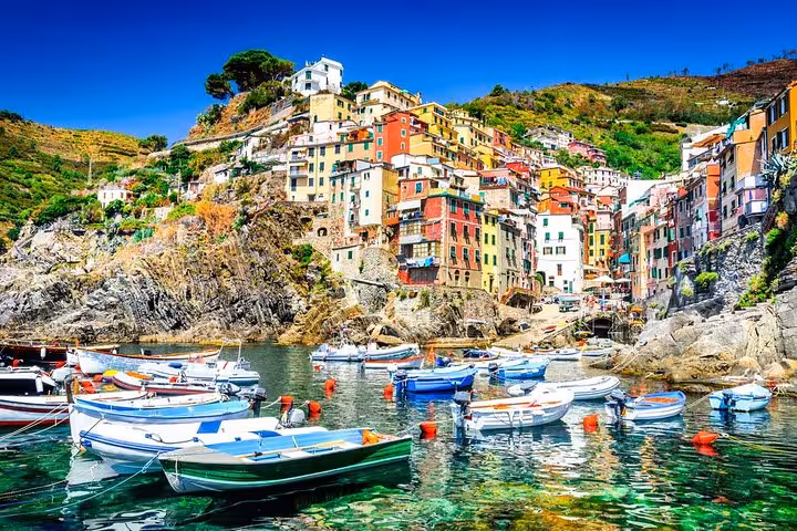 Colorful boats float in the vibrant harbor of Riomaggiore, Cinque Terre, showcasing stunning coastal cliffs and houses.