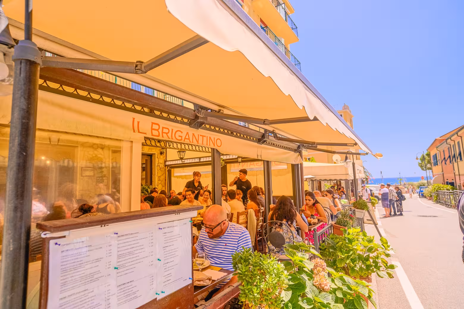 Outdoor diners enjoying Italian cuisine at a seaside restaurant in Cinque Terre with a view of the ocean.