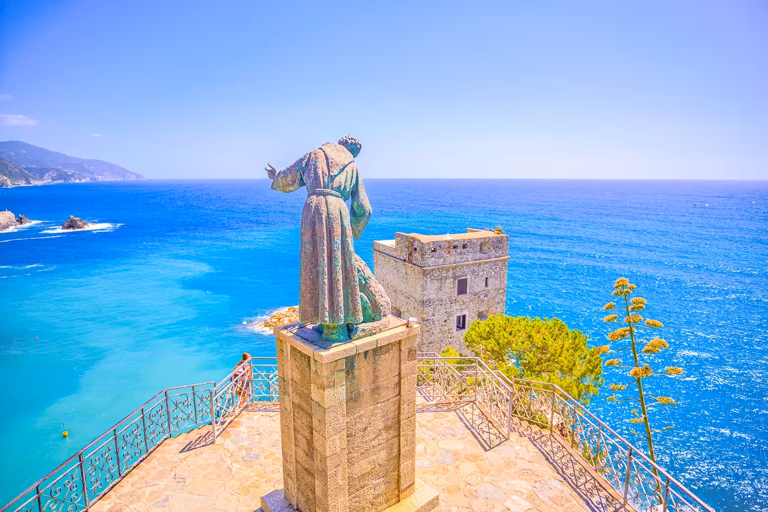 Statue overlooking the turquoise sea and historic building in Cinque Terre, Italy, on a sunny day.